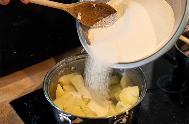 Přidávání mouky do hrnce s nakrájenými bramborami