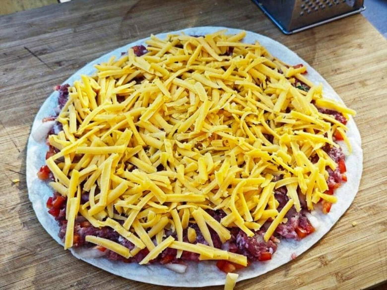 Tortilla s mletým masem, zeleninou a syrem před pečením.