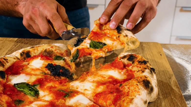 Čerstvá pizzy Margheritu se špeky bazalky je krájena na dřevěném prknu.