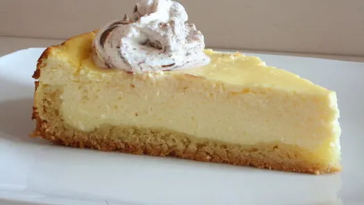 Kousek pečeného sýrového koláče se mascarpone na bílém talíři.