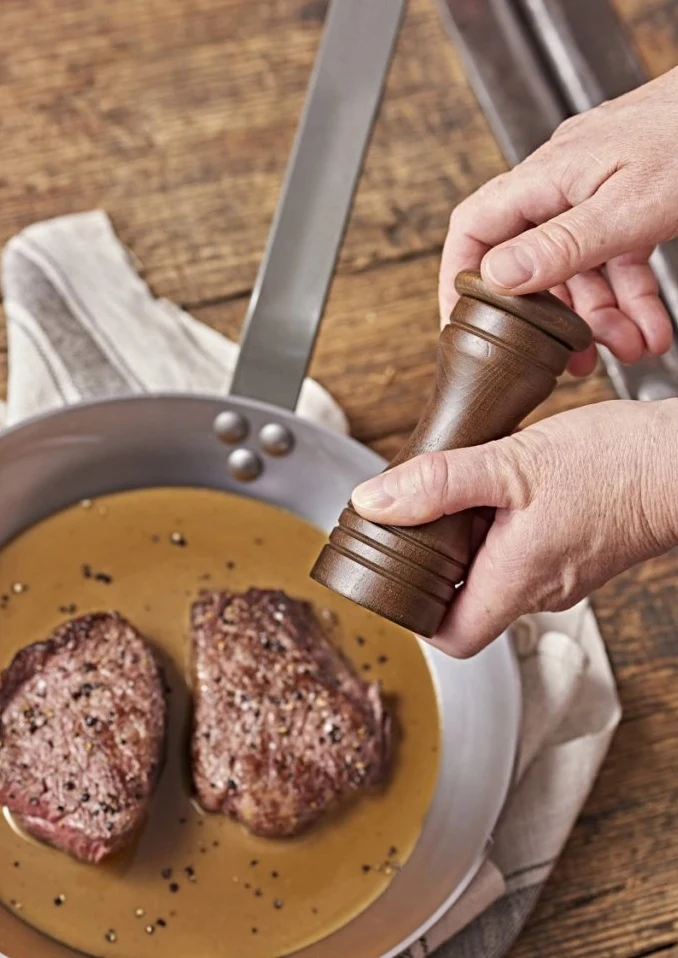 Osolení pečeného steaků pepřem v pánvi s omáčkou.