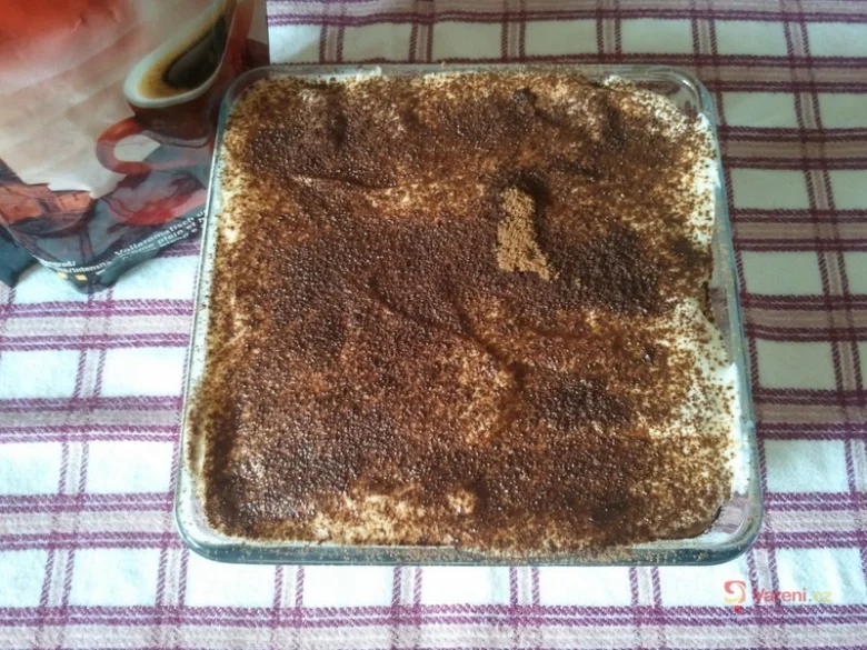 Tiramisu dezert v skleněné míse posypaný kakaem na pruhovaném ubrusu