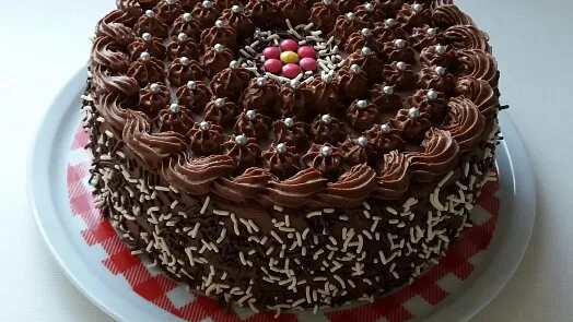 Čokoládová torta s ganache a stříbrnými kuličkami na bílém talíři.