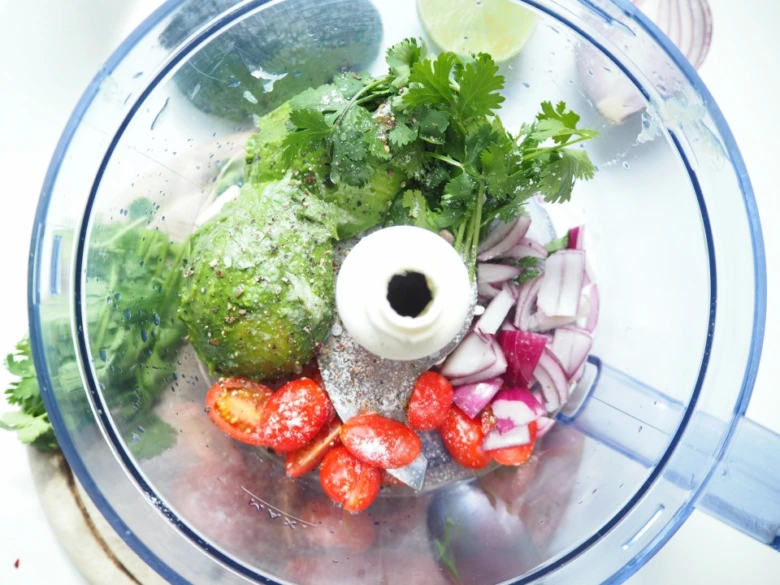Avokády, rajčata, cibule a koriandr v mixéru na guacamole.