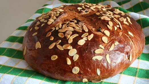 Zlatohnědý chlebík s mandlovými plátky na zeleno-bílé ubrus.