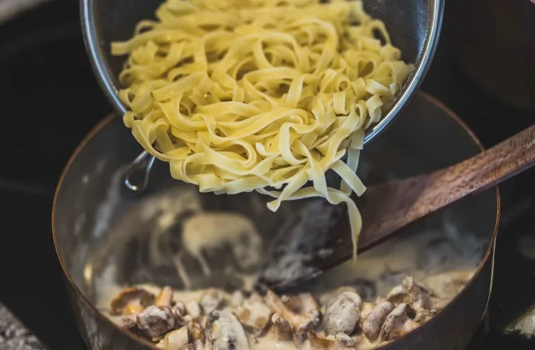Pasta s houbami v krémové omáčce se smíchává ve hrnci.