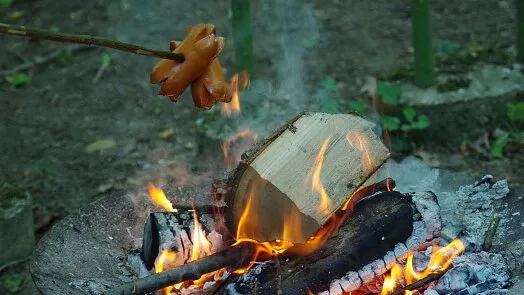 Klobásy se grilují nad ohněm s dýmem.