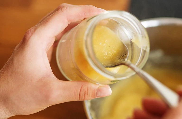Ruka drží sklenici s jablkovou přesnídávkou, kterou lžící překládá do misky.