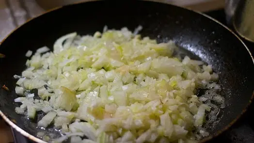 Smažené nakrájené cibule v pánvi pro recept na medailonky.