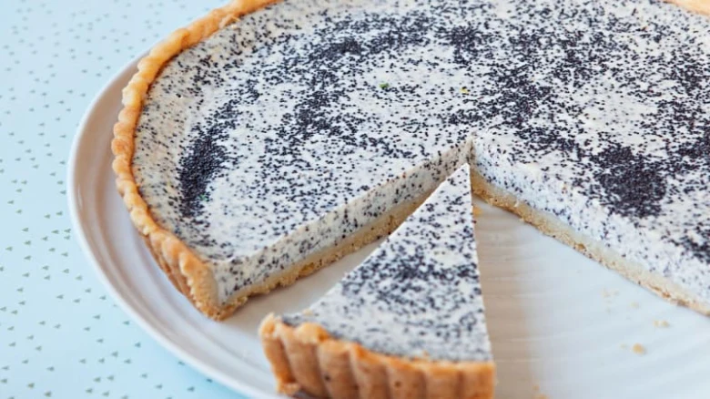 Kousek tvarohového cheesecaku s makem na bílém talíři.