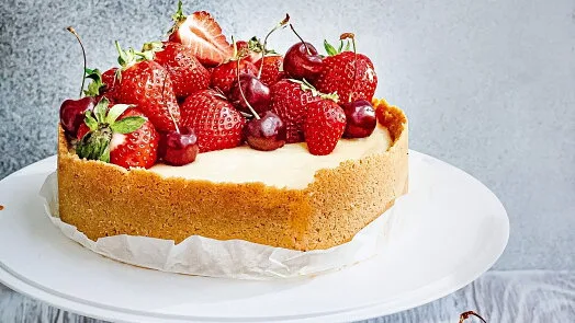 Nepečený cheesecake s jahodami a třešněmi na bílém talíři.