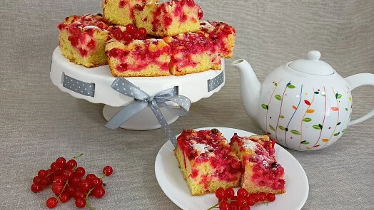 Kusky bublaniny s rybízem na bílém podstavci vedle čajníku.