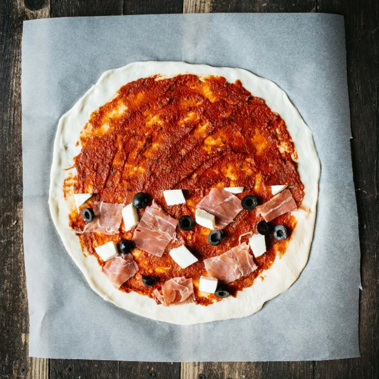Neupravená piza s ingrediencemi na sušeném droždí před pečením.