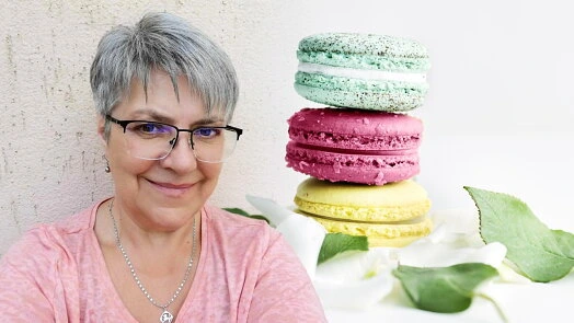 Žena se usmívá vedle barevného hromady makronů na bílých květech.