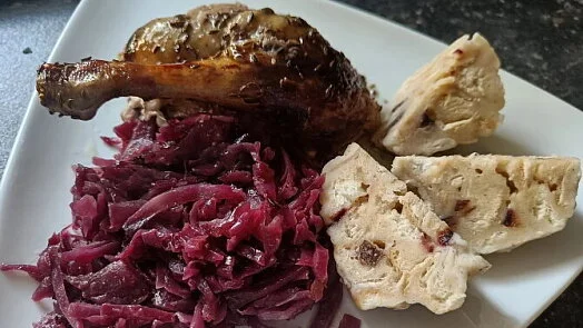 Pečená husa s červenou kapustou a knedlíky na talíři.