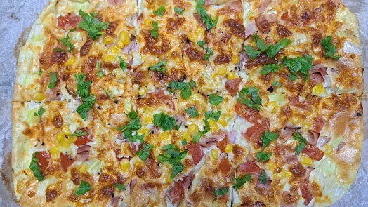 Hotová cottage pizza s uzeninou a kukuřicí na pečicím papíru.