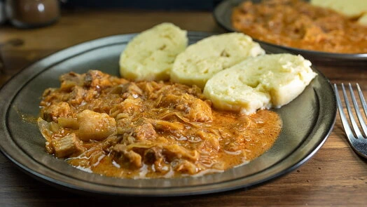 Hot český houskový knedlík s masovou omáčkou na talíři.