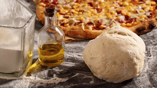 Kulka těsta na pizzu s olejem a moukou vedle hotové pizzy.