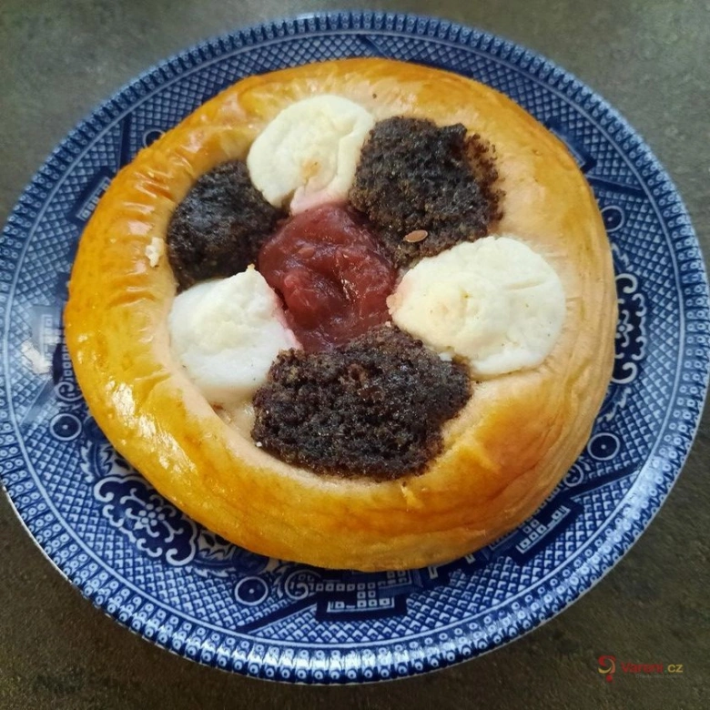 Koláč s tvarohovou náplní, makem a ovocným džemem na talíři.