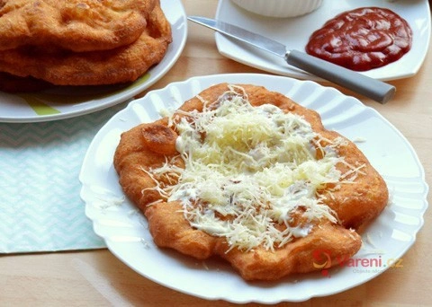 Zlatohnědý smažený langos s nastrouhaným sýrem podávaný na talíři.