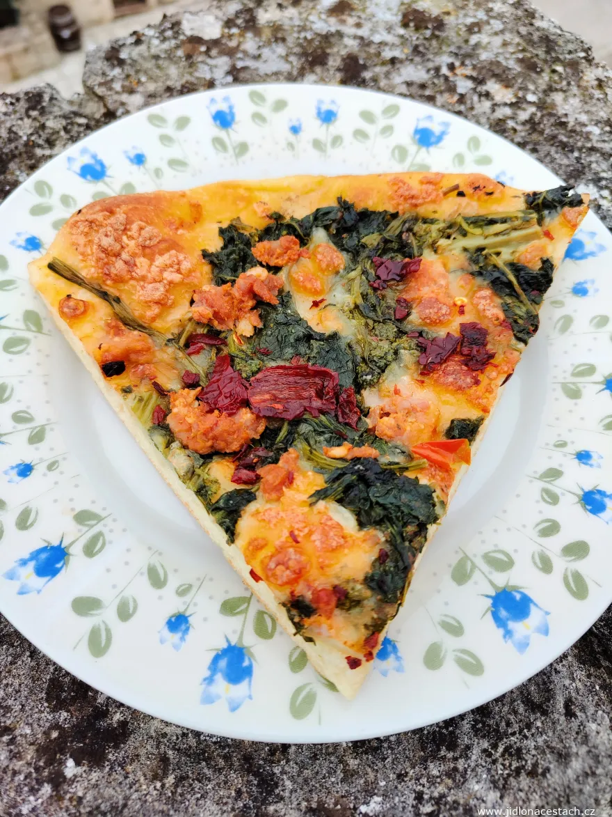 Kousek italské pizzy s listovými zeleninami na talíři.