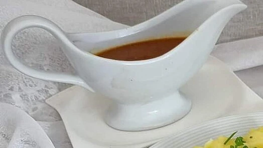 Bílá lžíce na omáčku s masovou šťávou vedle bramborového pyré.