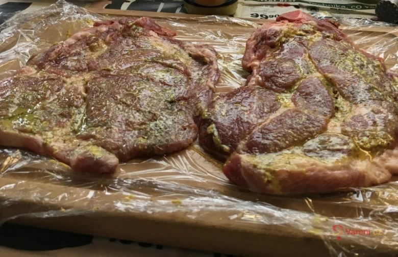 Dvě vepřové krkovice marinované na dřevěném prkénku.