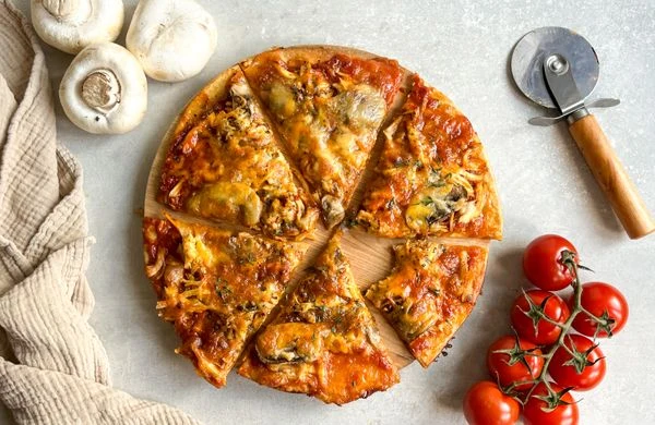 Připravená pita s žampiony, rajčaty a syrem na dřevěném podnosu.