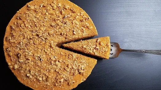 Medovník s ořechy na vrchu, z něho je vyndána jedna porce.