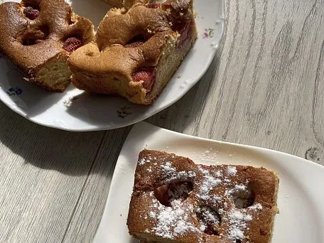 Kousky koláče s tvarohem a jahodami posypané cukrem.