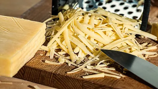 Kousek sýra vedle nastrouhaného sýru pro risotto.
