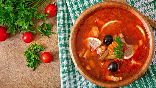 Dřevěná miska s ruským borščem ozdobená citrony, olivami a petrželkou.