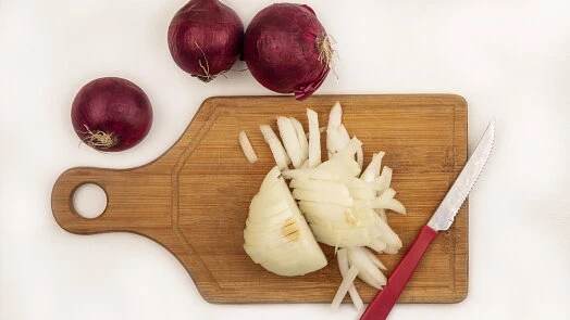 Červená cibule nakrájená na dřevěném prkénku s nožem.