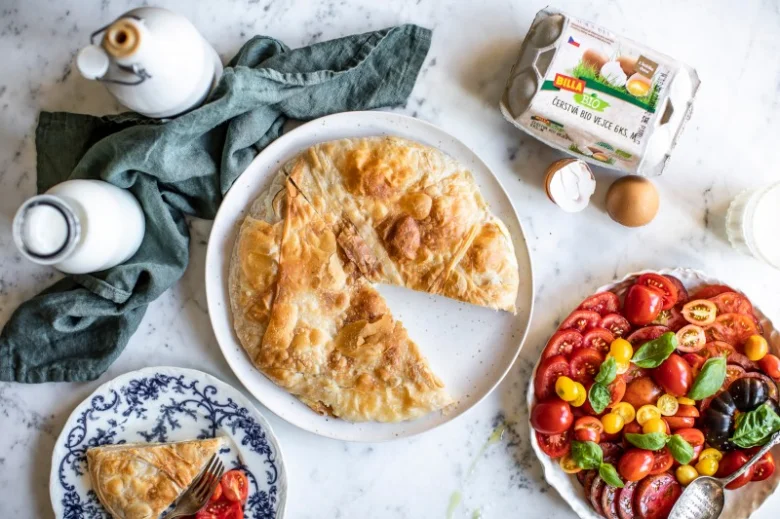 Burek z listového těsta s rajčatovou salátou na bílém talíři.
