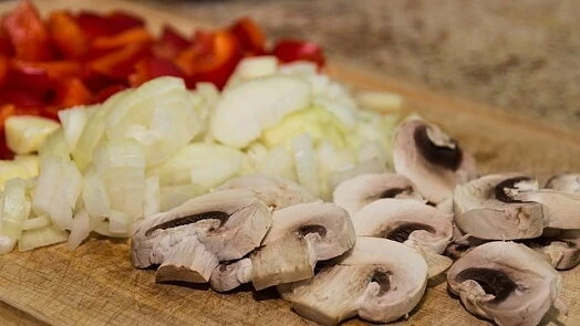 Nakrájené zelenina: paprika, cibule a houby na prkénku.