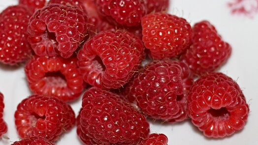 Čerstvé červené maliny v hromadě na bílém podkladu.