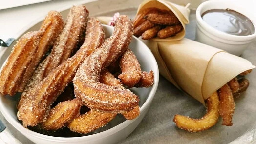 Churro s cukrem a čokoládovou omáčkou na talíři.