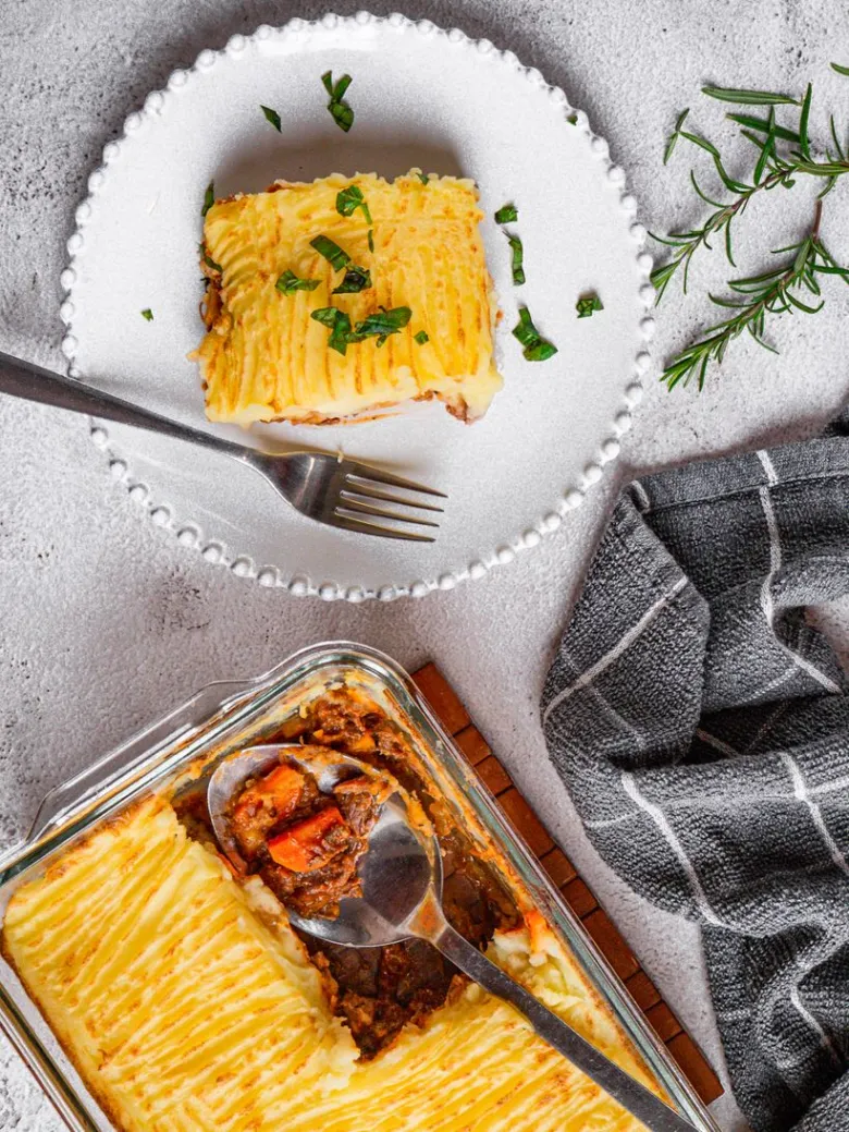 Kousek pastýřského koláče na talíři vedle pekáčku s masem.