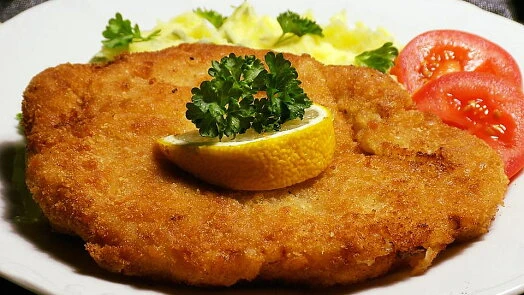 Zlatě hnědý řízek s citronem a petrželkou na talíři.