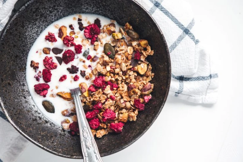 Domácí granola s mlékem, malinami a ořechy v hrnci.