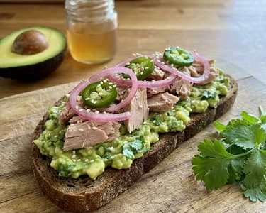 Avokádový toast s tuňákem, jalapeño a nakrájenou cibulí.