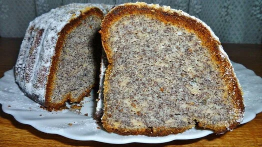 Kousek koláče s makem na bílé talíři posypaný moučkovým cukrem.