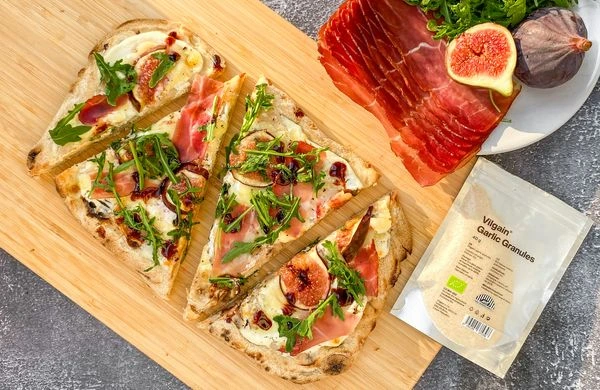 Italská pizza s fíky, prosciutto a rukolou na dřevěném prknu.