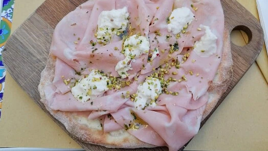 Neupravená domácí pizza s uzeninou na dřevěném prknu.