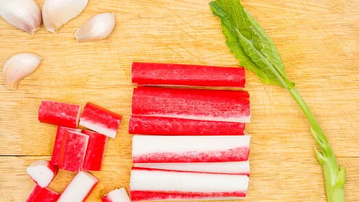 Nakrájené surimi tyčinky s česnekem na dřevěném prknu pro pomazánky