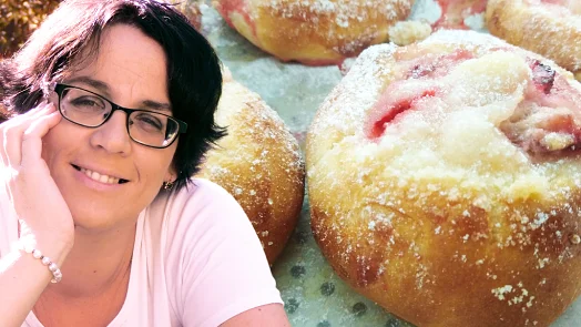 Žena se usmívá vedle kynutých koláčů se švestkami.