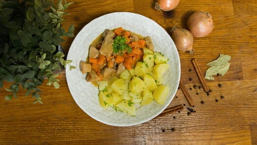 Dušené vepřové maso s mrkví a bramborou podávané na talíři.