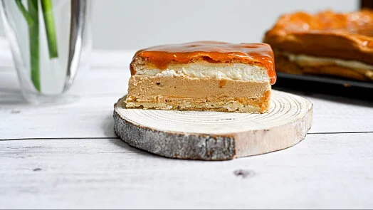 Kousek vrstveného slanokaramelového koláče na dřevěném podstavci.