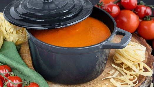 Červená rajská omáčka v hrnci s těstovinami a čerstvými rajčaty.