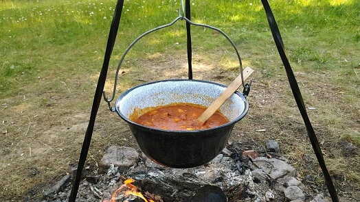 Červený guláš se vaří v hrnci nad ohněm venku.